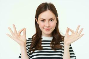 Portrait of woman smiling with confidence, showing okay, zero sign, meditating, standing over white background photo