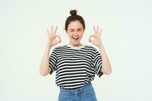 Excellent choice. Smiling stylish young woman, showing okay, ok gesture, zero sign, standing over white background photo