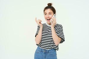 Happy young woman talks on mobile phone, chats on telephone, uses smartphone, stands over white background photo