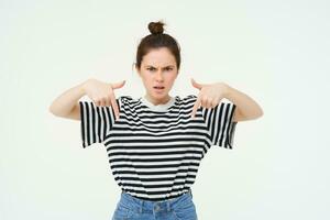 Angry woman frowning, pointing fingers down at something bad and disappointed, isolated over white background photo