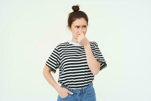 Young woman shuts her nose with fingers from disgusting smell, isolated on white background photo