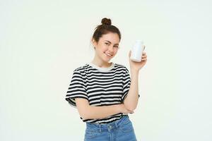 Young smiling woman recommends vitamins, shows bottle with dietary supplements, looks healthy and happy, isolated over white background photo