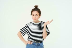 Portrait of confused girl, shrugging should and raising one hand up, looks puzzled, cant understand something, standing over white background photo