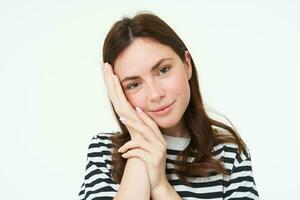 Portrait of tender, beautiful young woman, touches her clear, glowing skin, without blemishes or acne, concept of makeup and cosmetology, white background photo