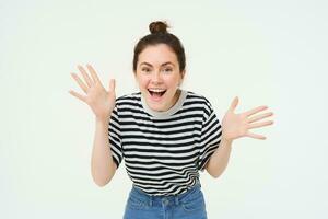 Portrait of happy, beautiful girl makes jazz hands, tells big news, revelation, introduces surprise, stands over white background photo