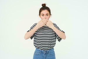 Image of shocked woman, covers her mouth, looks surprised, stands over white background photo