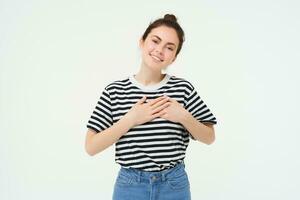 Portrait of smiling modern woman, holding hands on heart, says thank you, expresses her warm feelings, white background photo