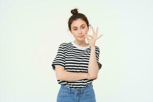 Portrait of brunette woman seals her mouth with promise not to tell anyone, zipping gesture, standing over white background photo