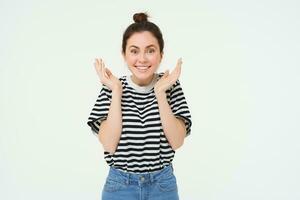 Portrait of woman reacts to amazing news, claps hands and smiles, pleased by smth, stands over white background photo
