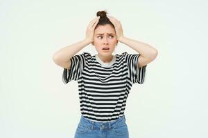 imagen de joven mujer en pánico, mirando preocupado, gritando, participación manos en cabeza, reaccionando a malo noticias, desastre, en pie terminado blanco antecedentes foto