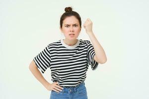 Image of angry woman threatening, shaking fist with disapproval, scolding someone, standing over white background photo