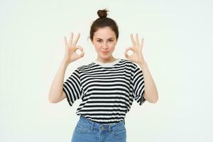 No problem, excellent choice. Smiling, confident young woman, showing okay, ok sign, zero gesture, recommends product, stands over white background photo