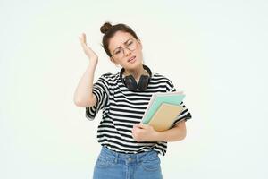 Image of upset young woman, student in glasses complains at difficult task at university, holding notebooks, forgot to do something, white background photo