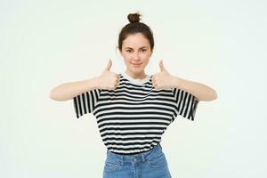 Portrait of confident, beautiful woman, showing thumbs up, recommends product, likes and approves, stands over white background photo