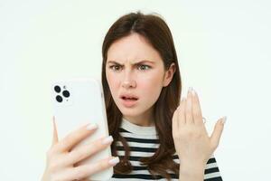 retrato de confundido, enojado mujer ceñudo, leyendo texto en teléfono inteligente, acecho vídeo en móvil teléfono con conmocionado, perplejo cara expresión, aislado en blanco antecedentes foto