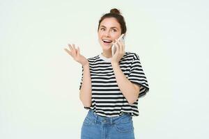 Happy young woman talks on mobile phone, chats on telephone, uses smartphone, stands over white background photo