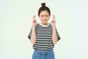 retrato de esperanzado joven mujer, hace desear, cruzar dedos para bueno suerte, deseando, anticipando, en pie terminado blanco antecedentes foto