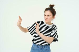 Image of woman expressing aversion, dislike something, looks apalled, extends hands forward in defensive gesture, rejecting, refusing, standing over white background photo