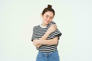 self-care and love. Young beautiful woman hugs herself, embraces own body and smiles, stands over white background photo