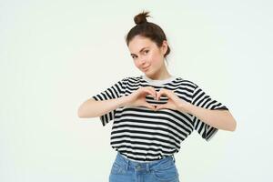 Beautiful european woman, shows heart sign, expresses her love and affection, flirting, standing over white background photo