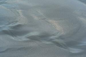 borroso natural fondo, agua fluye a lo largo el playa desde negro volcánico arena foto