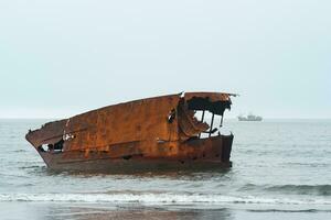 rusty shipwreck against a foggy seascape with a ship in the distance photo