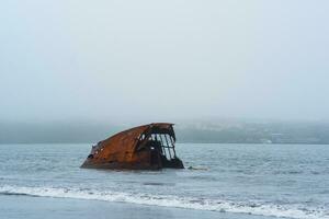 oxidado naufragio, permanece de un Embarcacion lavado en tierra en contra un brumoso costa foto