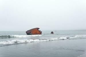 rusty shipwreck, fremains of a ship washed ashore against a foggy seascape photo