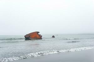 oxidado naufragio, fragmentos de un Embarcacion lavado en tierra en contra un brumoso marina foto