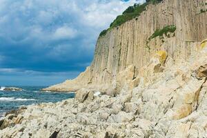 ocean shore with rocks of columnar basalt, Cape Stolbchaty on Kunashir Island photo