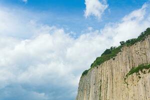 top of columnar volcanic basalt cliff against the background of the sky with clouds photo