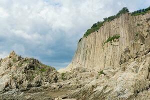 high coastal cliff formed by solidified lava stone columns, Cape Stolbchaty on Kunashir island photo