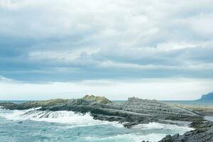 rocky seashore formed by columnar basalt against the backdrop of a stormy sea, coastal landscape of the Kuril Islands photo