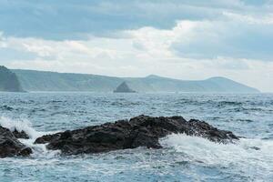 seascape with distant wooded shore on a background and rocks in the surf on a foreground, Kunashir island landscape photo