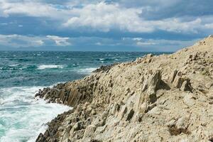 rocky seashore formed by columnar basalt against the backdrop of a sea, coastal landscape of the Kuril Islands photo