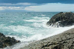 rocky seashore formed by columnar basalt against the surf, coastal landscape of the Kuril Islands photo