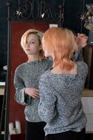 adolescente niña mira en el espejo interior, cuidadosamente examina su peinado foto