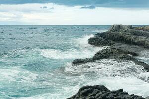 rocky seashore formed by columnar basalt against the backdrop of a stormy sea, coastal landscape of the Kuril Islands photo