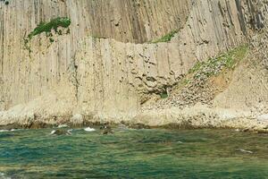 natural landscape with a sheer cliff folded columnar basalt on the seashore photo