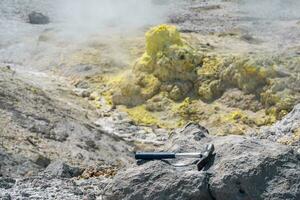 geological hammer on the rock against the backdrop of an steaming fumarole on the slope of a volcano photo