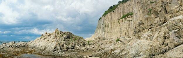 panorama with coastal cliff formed by solidified lava stone columns, Cape Stolbchaty on Kunashir island photo