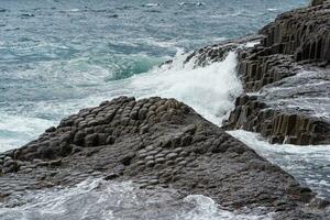 severe rocky seashore composed of columnar basalt against the stormy sea, coastal landscape of the Kuril Islands photo