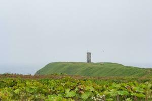 abandonado faro en un alto herboso promontorio encima un brumoso mar foto