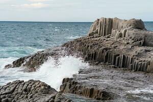 rocks formed by columnar basalt among the sea surf, Cape Stolbchaty on Kunashir Island photo