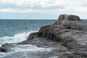 rocks formed by columnar basalt among the sea surf, Cape Stolbchaty on Kunashir Island photo