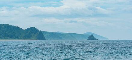 seascape with distant wooded shore with volcanic rocks, Kunashir island photo