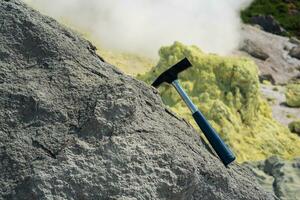 geological hammer in the rock against the backdrop of an steaming fumarole on the slope of a volcano photo