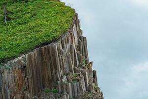 fragmento de un acantilado formado por de columna basalto con lozano césped en parte superior en contra el cielo foto