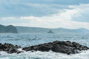 seascape with distant wooded shore on a background and rocks in the surf on a foreground, Kunashir island landscape photo