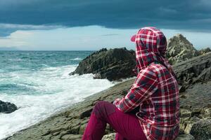 traveler sits on the shore of a stormy sea, on a natural pavement made of columnar granite photo